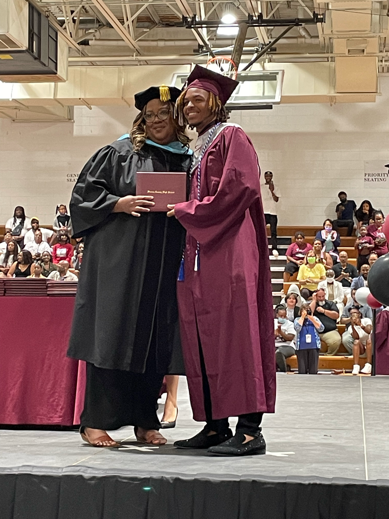 Principal Dr. Lewis posing with a graduate as she hands him his diploma