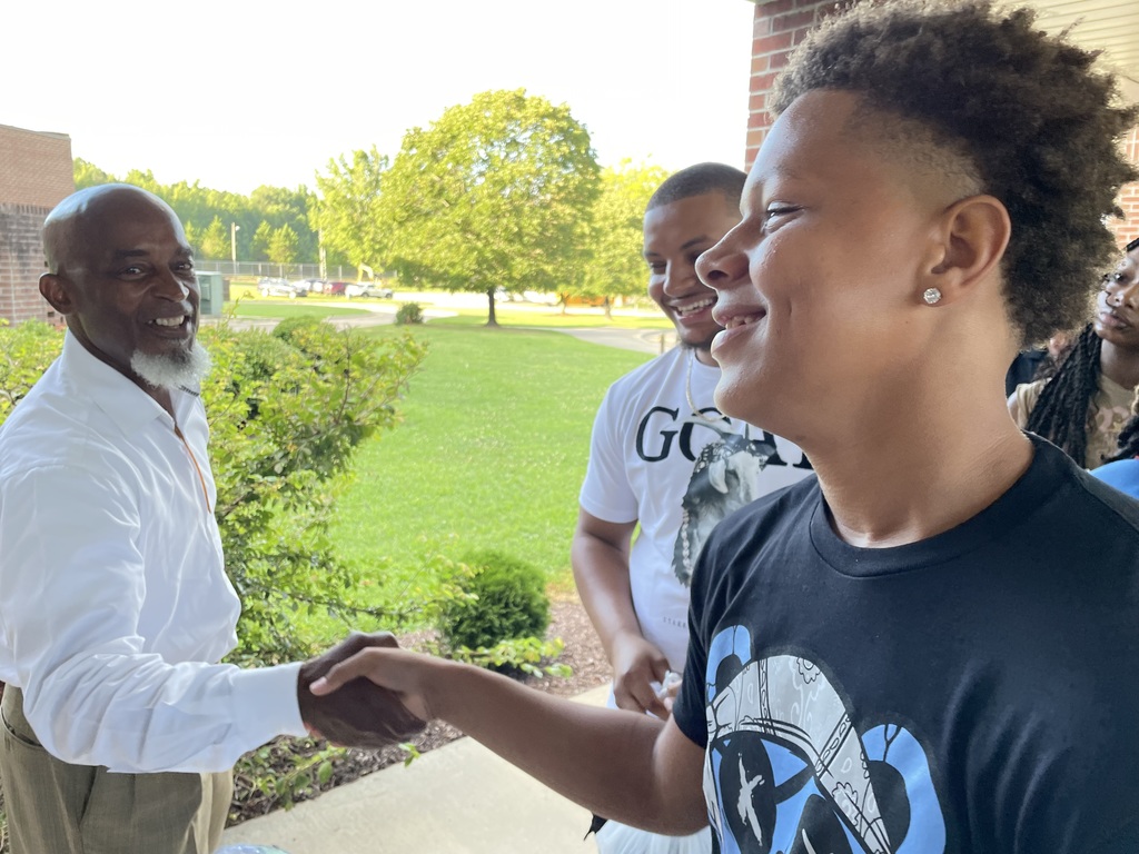 A greeter and a student shake hands and exchange smiles outside of school